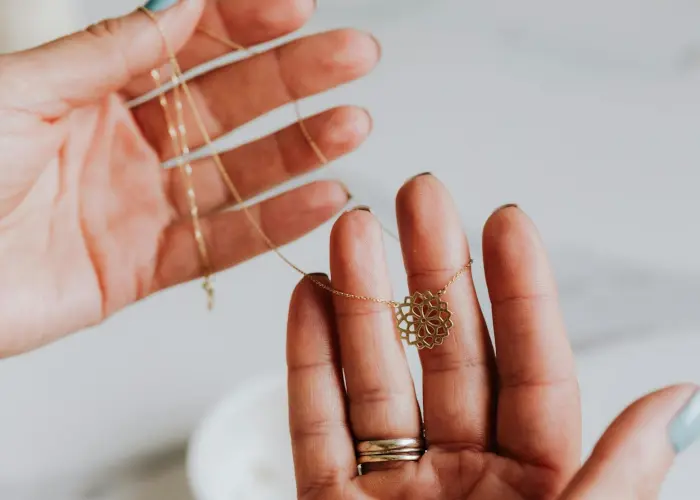 A pair of hands holding a delicate gold necklace with a geometric pendant, showcasing intricate handmade jewelry