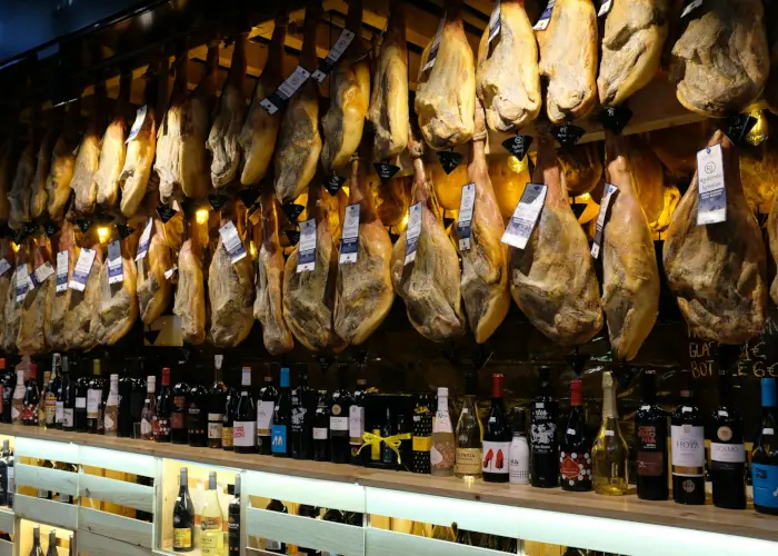 A delicatessen with rows of Iberian ham (jamón) hanging from the ceiling above a display of assorted wine bottles