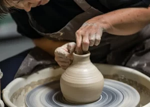 A potter shaping a clay vase on a spinning pottery wheel, with hands covered in wet clay and wearing a dark apron