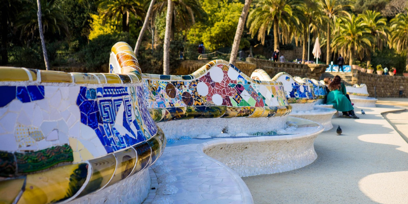 Colorful mosaic benches at Park Güell, Barcelona, surrounded by palm trees.