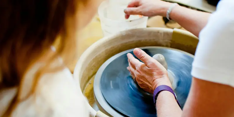 Two women shaping clay on a pottery wheel during a hands-on ceramics workshop.