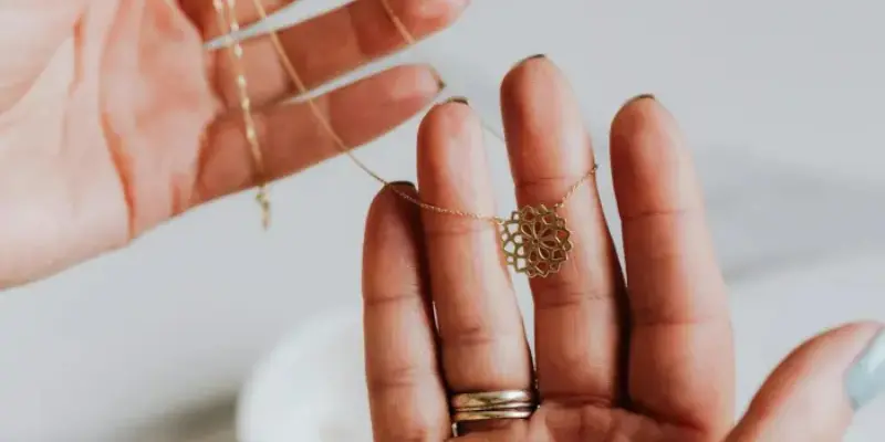 A pair of hands holding a delicate gold necklace with a geometric pendant, showcasing intricate handmade jewelry