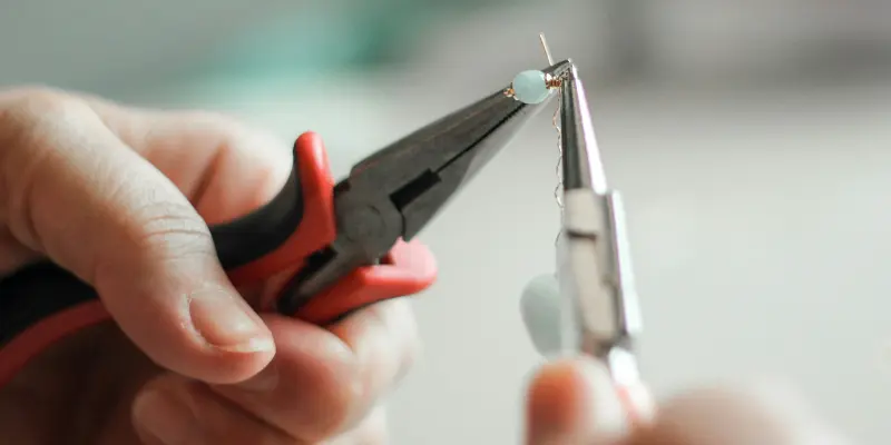Hands using pliers to craft handmade jewelry with small beads
