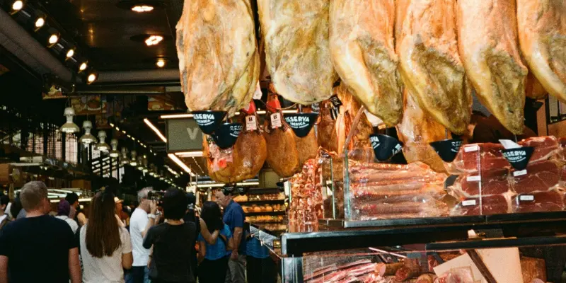 Hanging cured Jamón legs and packaged meats displayed in a busy Spanish market in Barcelona