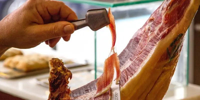 Hand slicing a thin piece of Spanish Jamón Ibérico from a cured ham leg