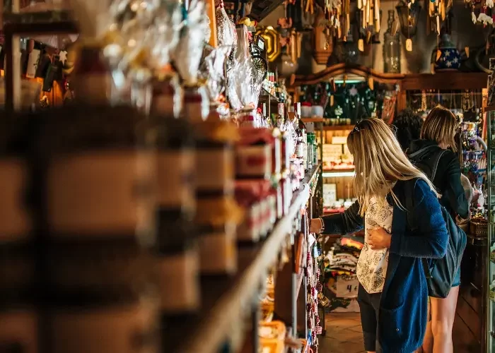handicraft-shopping-barcelona Woman browsing through shelves filled with artisanal products in a warmly lit handicraft store, surrounded by jars, souvenirs, and decorative items
