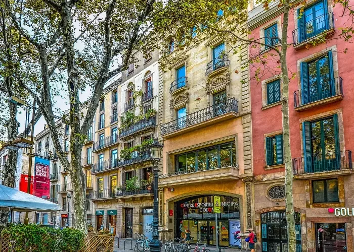 shopping-street-barcelona Vibrant shopping street in Barcelona lined with colorful historic buildings, featuring balconies with greenery, large trees, and people strolling past shops